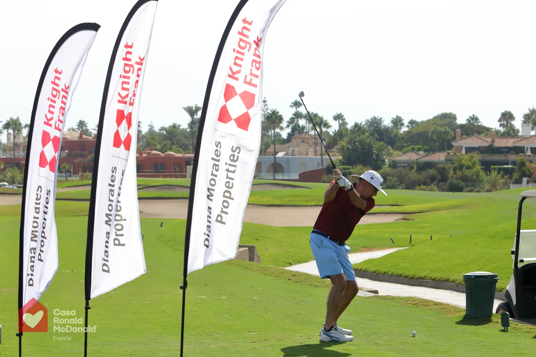 Salida al tiro del torneo de golf solidario con las banderolas de Diana Morales Properties y Knight Frank en Guadalmina